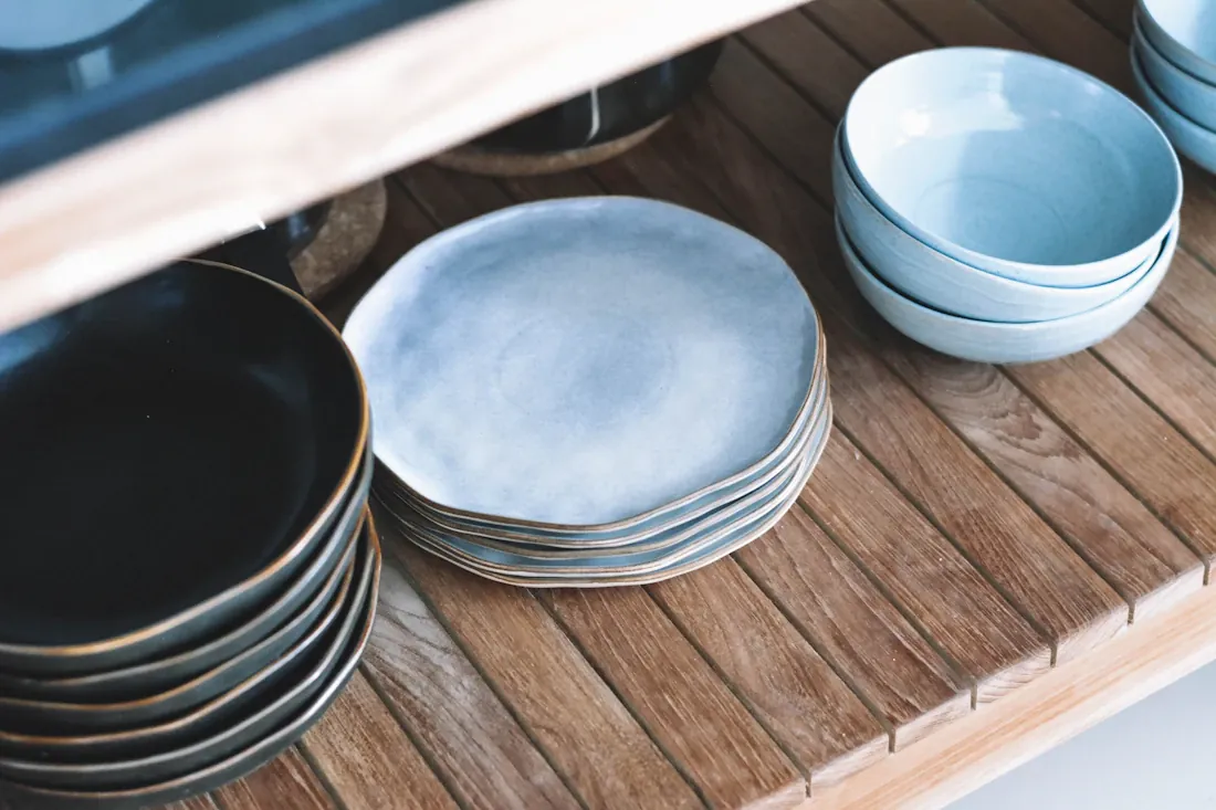 Blue handmade ceramic bowls and plates displayed on a wooden shelf